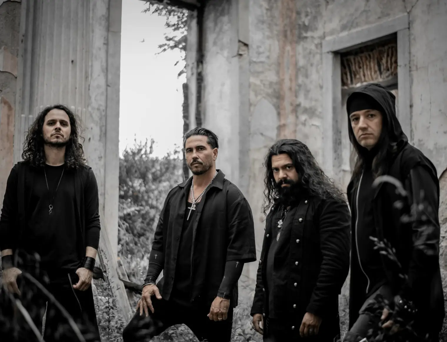 Os quatro músicos dos Maledictus vestidos de preto, de pé entre as paredes de um edifício em ruínas